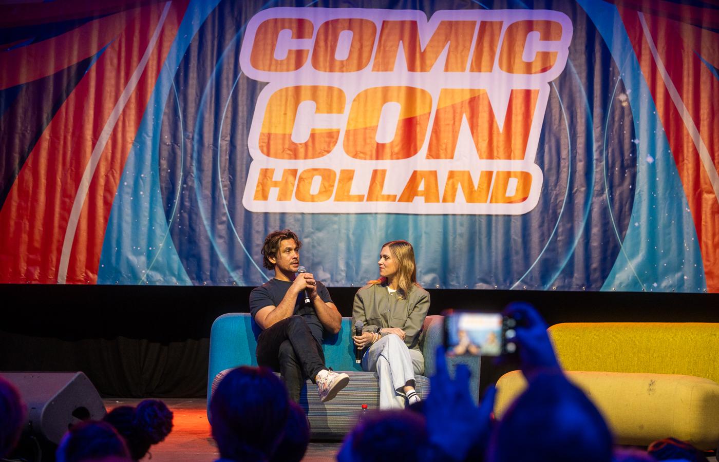 Two panelists speaking on stage beneath a large Comic Con Holland backdrop
