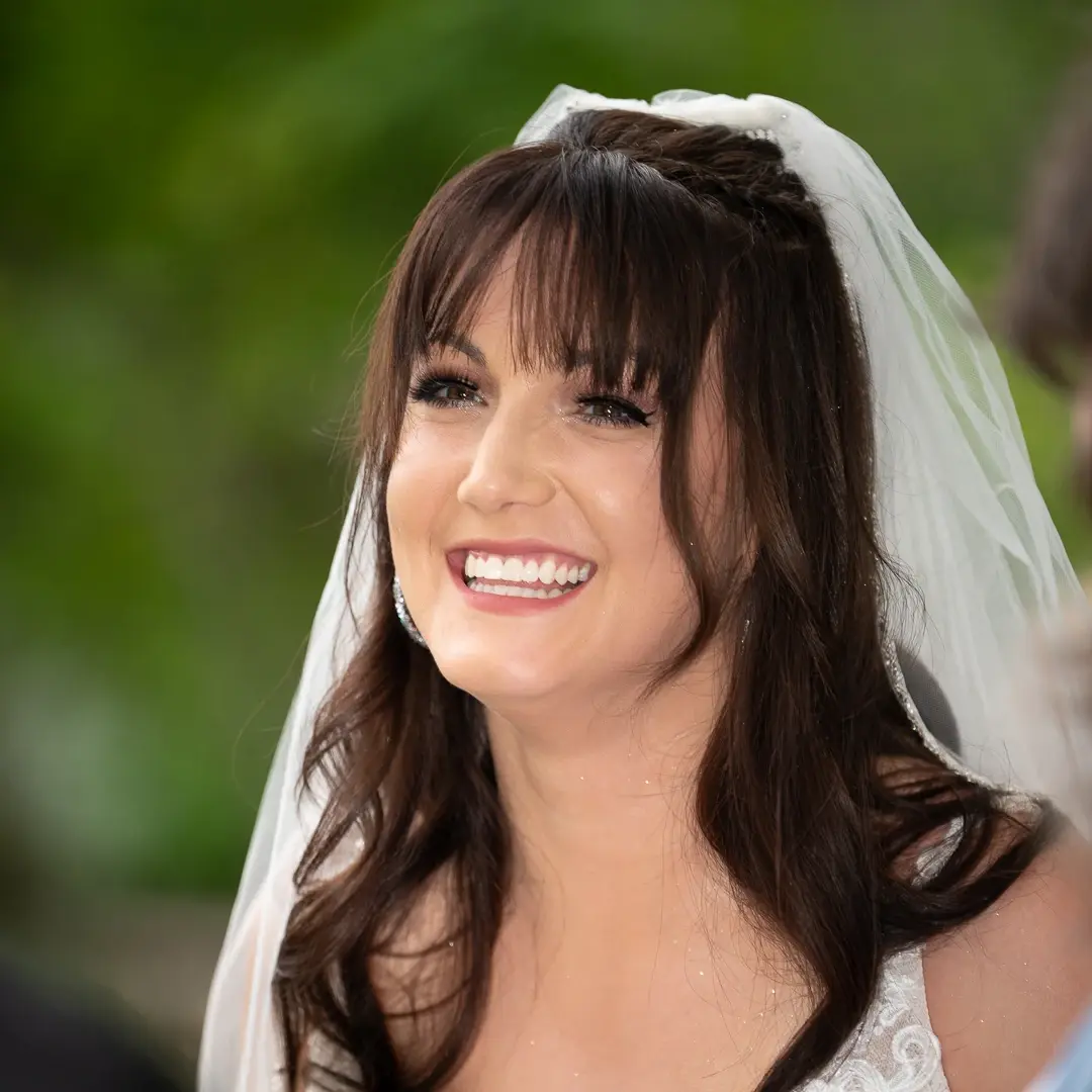 Bride in a white veil laughing warmly against a soft green background