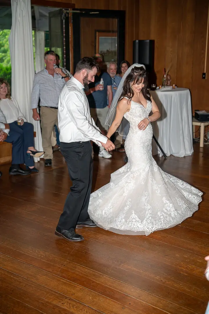 Bride and groom sharing a first dance on a wooden floor while guests look on