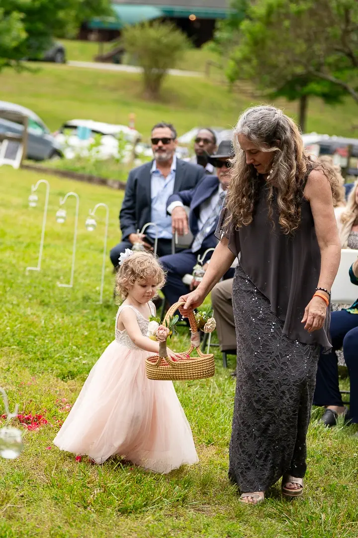 Flower girl scattering petals from a basket while being guided down a grass aisle