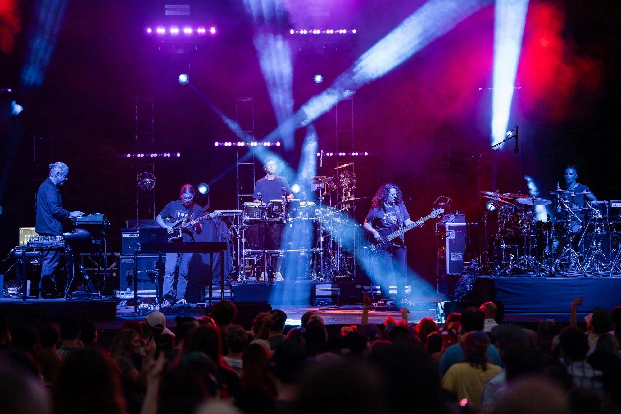 Full stage bathed in purple haze as spotlight beams cross over a silhouetted crowd
