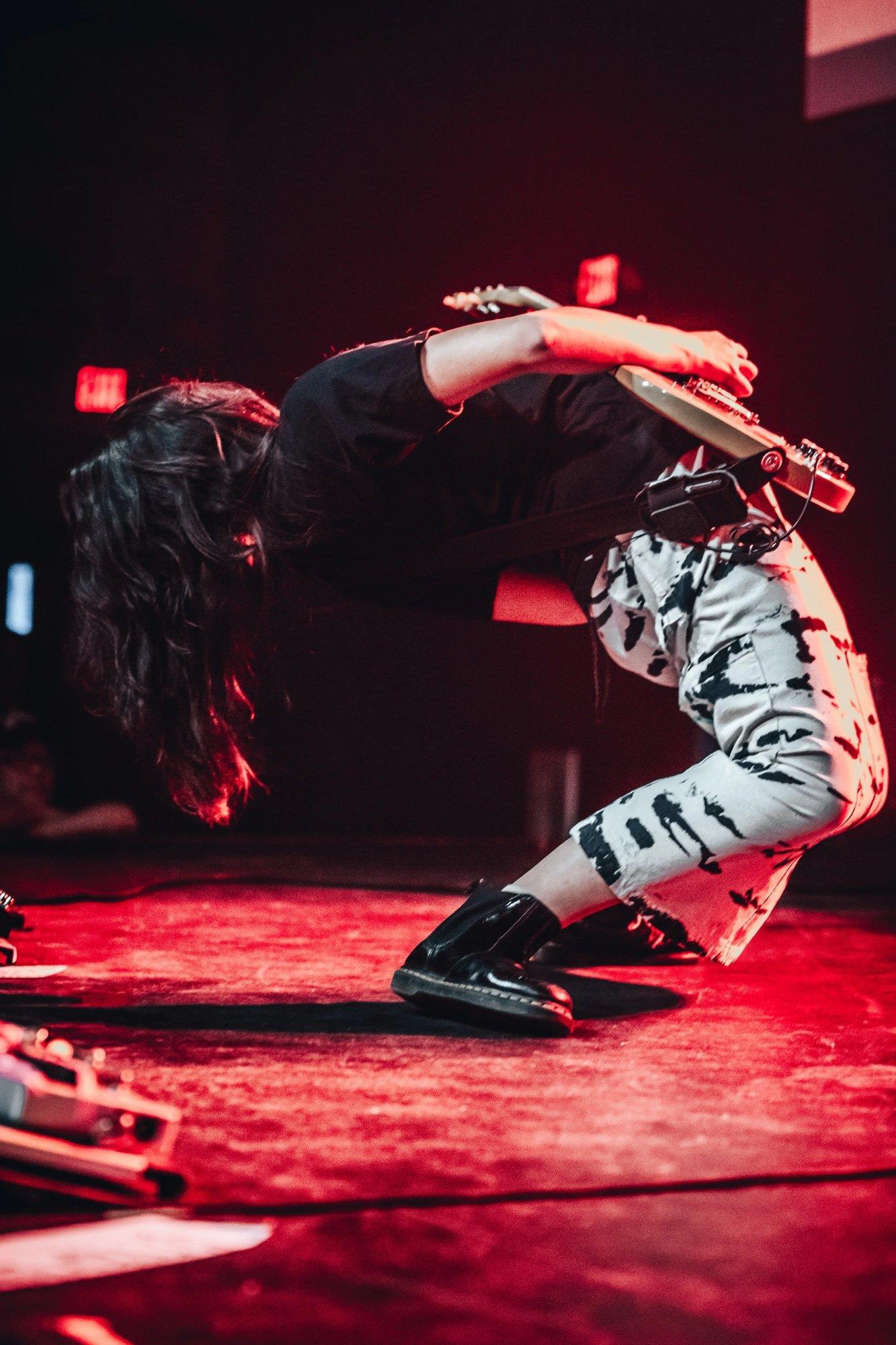 Guitarist bending fully backward mid-riff with the stage flooded in red light