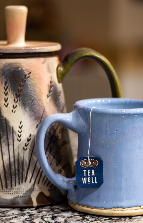 Handmade ceramic teapot and blue mug with tea bag tag on a granite counter